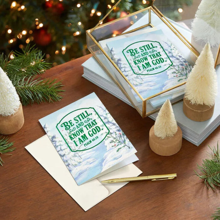 Greeting cards with 'Be Still and Know That I Am God' text on a festive table with Christmas decorations.
