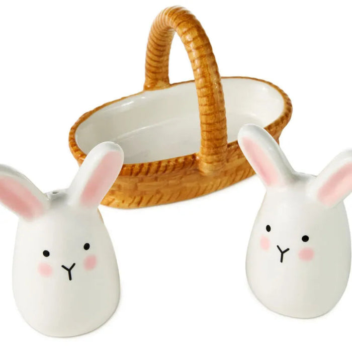 Two white ceramic rabbit salt and pepper shakers with a wicker basket in the background.