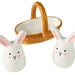 Two white ceramic rabbit salt and pepper shakers with a wicker basket in the background.