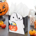 Halloween-themed gift bag with ghost design and candy on a table with pumpkins and jars.