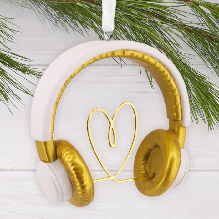 Decorative ornament shaped like gold headphones with a heart made from wire, hanging against a white background with greenery.
