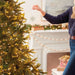 Person decorating a Christmas tree with lights and ornaments in a festive living room.