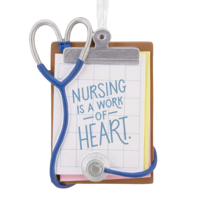 Decorative ornament with stethoscope and clipboard displaying 'Nursing is a work of heart' text on a white background.