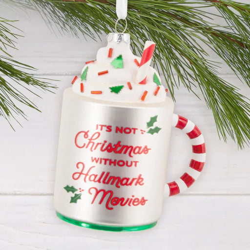 Decorative ornament shaped like a mug with candy cane handle, whipped cream, and candy canes on a white background.