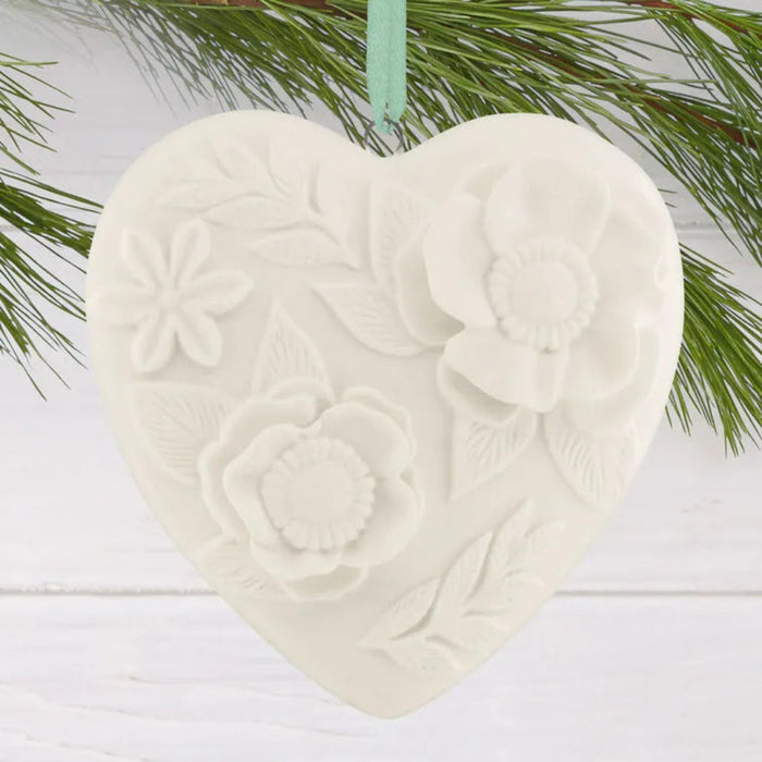 Heart-shaped ceramic ornament with floral patterns hanging on a branch.