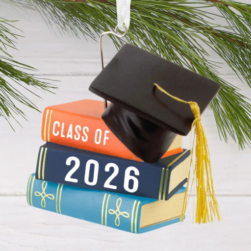 Graduation-themed ornament with books and a cap, featuring 'Class of 2026', on a white background.
