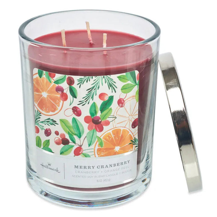 Candle with a decorative label featuring cranberry and orange fruits and a silver lid on a white background