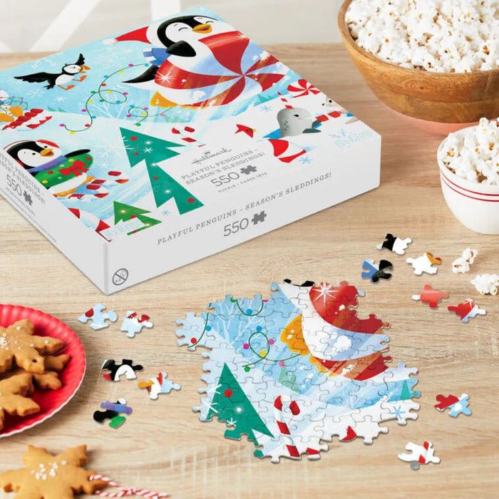 Puzzle box with Christmas- penguin themed design, puzzle pieces on a table with cookies and popcorn.