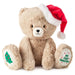 Beige teddy bear with a Santa hat and 'My First Christmas' paw pads on a white background