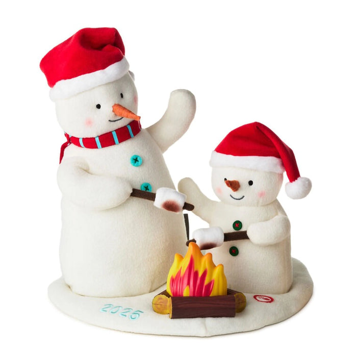 Two snowmen by a campfire, one larger and one smaller, on a white background. 2025 embroidered on the base of the Plush Snowman with lights and music. 