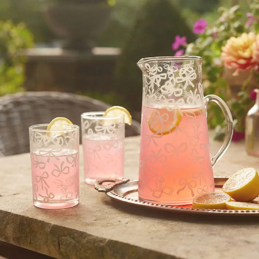 Pink lemonade in glasses and a pitcher on a stone surface with a garden background