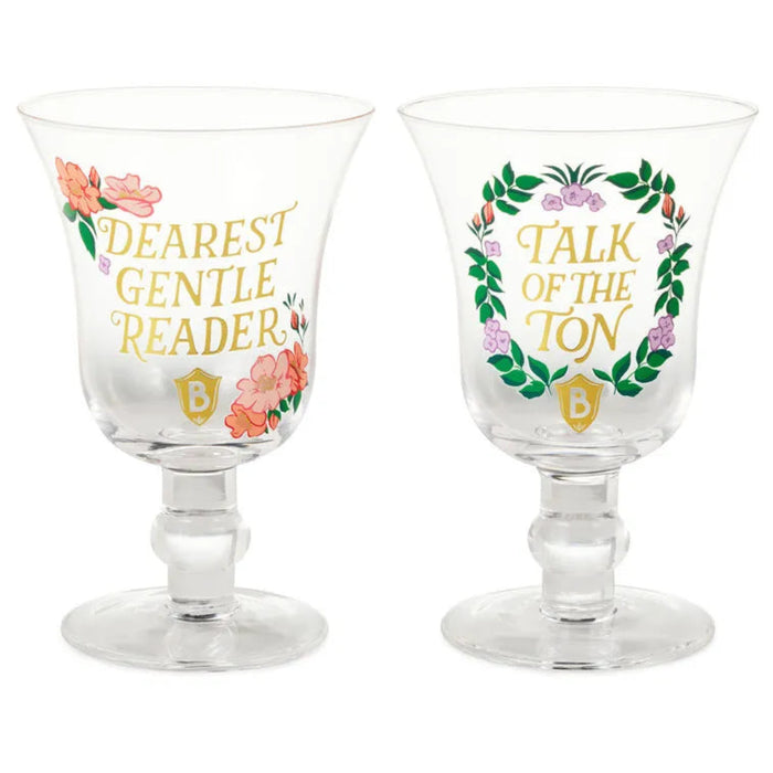 Two clear Bridgerton goblet glasses shown side by side on a white background, one reading ‘Dearest Gentle Reader’ and the other ‘Talk of the Ton,’ both decorated with gold lettering and floral wreath designs.”