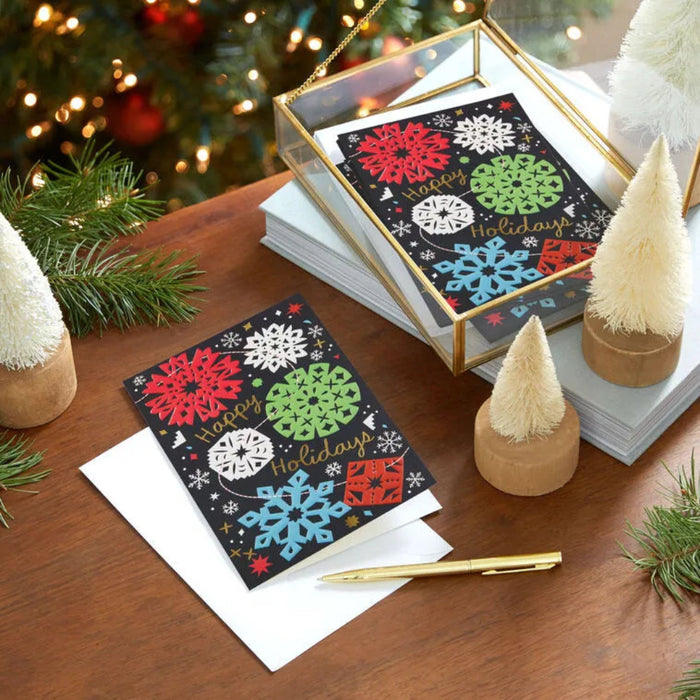 Holiday greeting cards with colorful snowflakes on a wooden table with Christmas decorations.