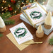 Christmas cards with penguin design on a wooden table with festive decorations.