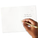 Hand holding a gold pen over a white card with text on a white background