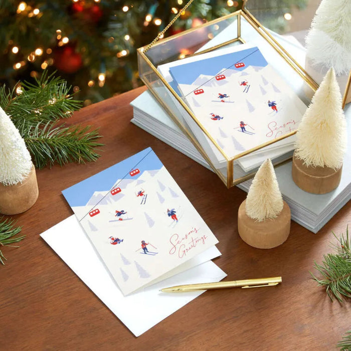 Stack of greeting cards with skiing design on a wooden surface with Christmas decorations.