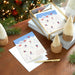 Stack of greeting cards with skiing design on a wooden surface with Christmas decorations.