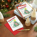 Christmas cards with festive designs on a wooden table with decorative elements.