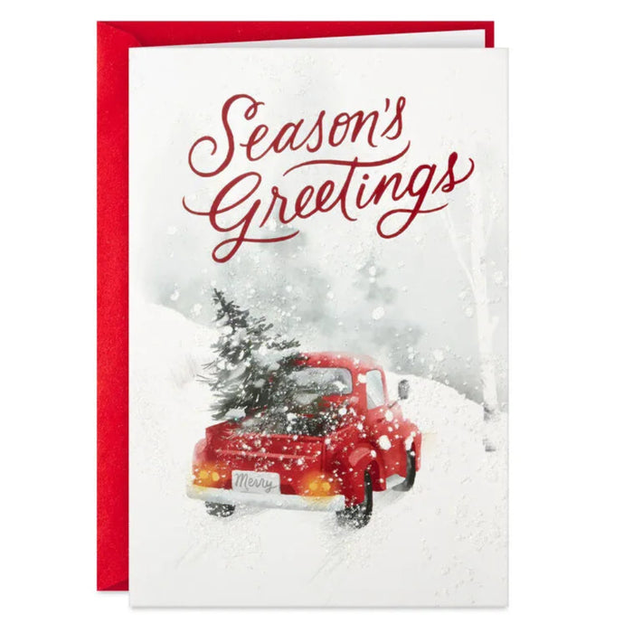 Christmas card with a red truck carrying a Christmas tree in the snow, featuring 'Season's Greetings' text.
