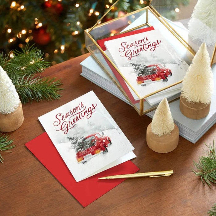 Stack of Christmas cards with 'Season's Greetings' on a wooden table with festive decorations.