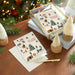 Holiday cards with Christmas-themed designs on a wooden surface with decorative elements.