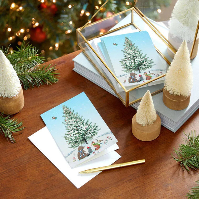Christmas cards with a snowy tree design on a wooden table with decorative items.
