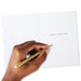 Hand holding a gold pen over a white card with 'Merry Christmas' text.