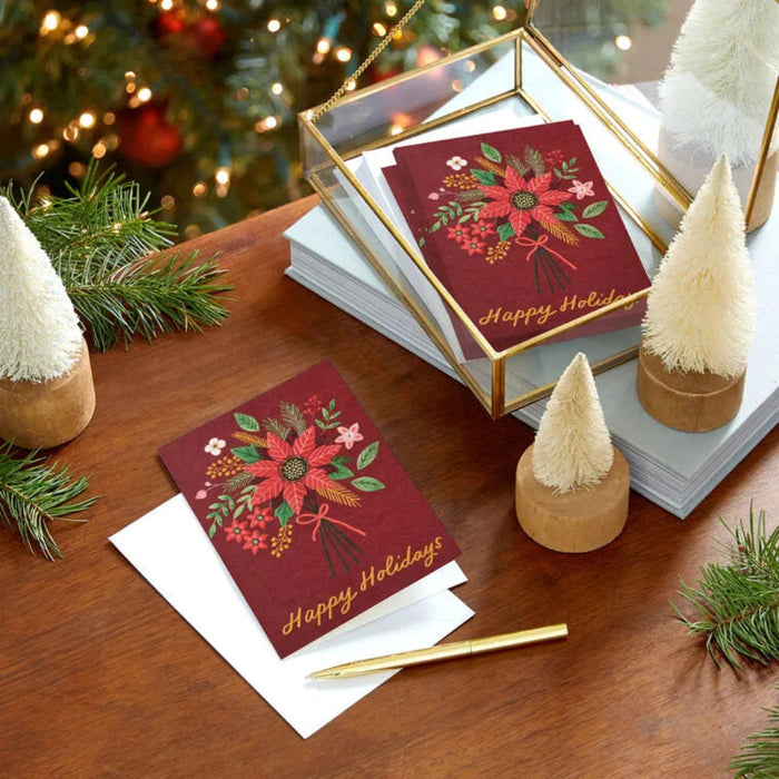 Christmas cards with poinsettia design on a wooden surface with decorative trees and lights.