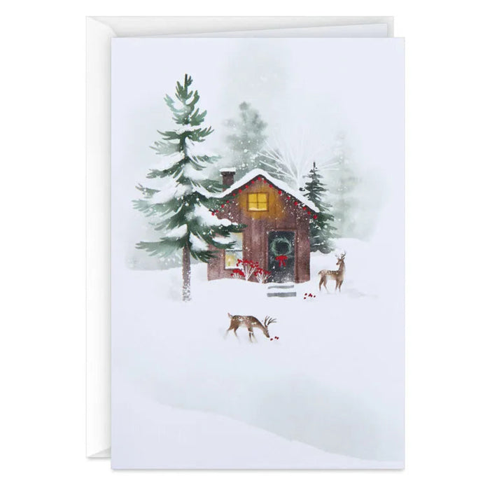 Greeting card with a winter scene featuring a cabin, trees, and deer.