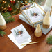 Stack of Christmas cards with a gold pen and decorative trees on a wooden surface.
