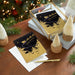 Decorative greeting cards with gold and black design on a wooden surface with Christmas decorations.