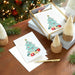 Stack of Christmas cards with a decorative tree design on a wooden surface with festive decorations.