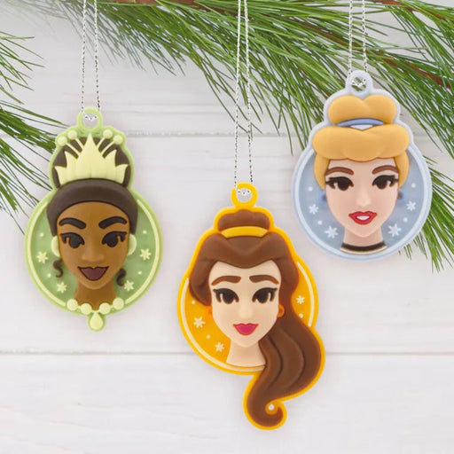 Three princess-themed  mini Christmas ornaments hanging on a  Christmas tree branch.