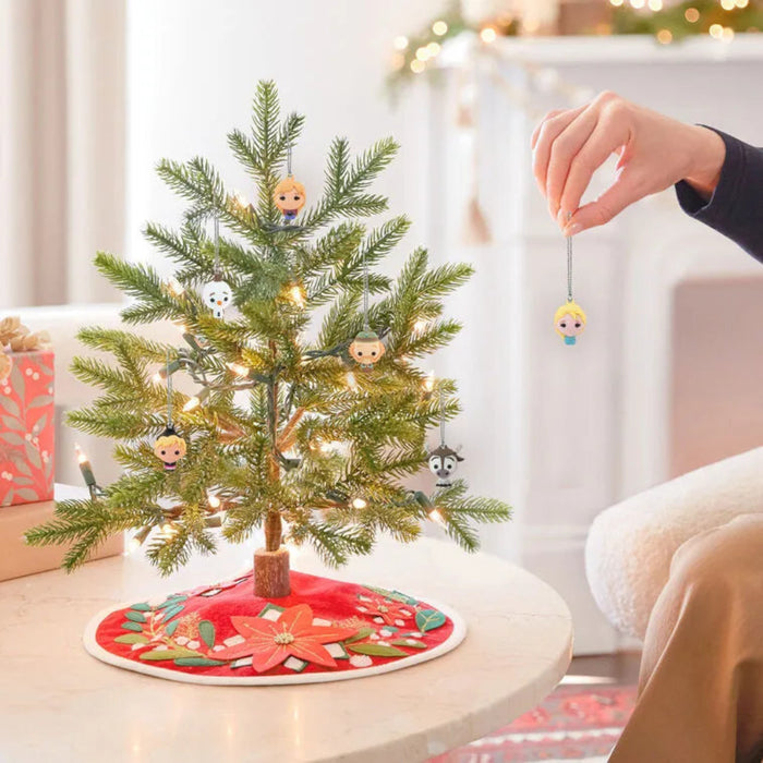 Small decorated Christmas tree with ornaments on a table, surrounded by festive decorations.