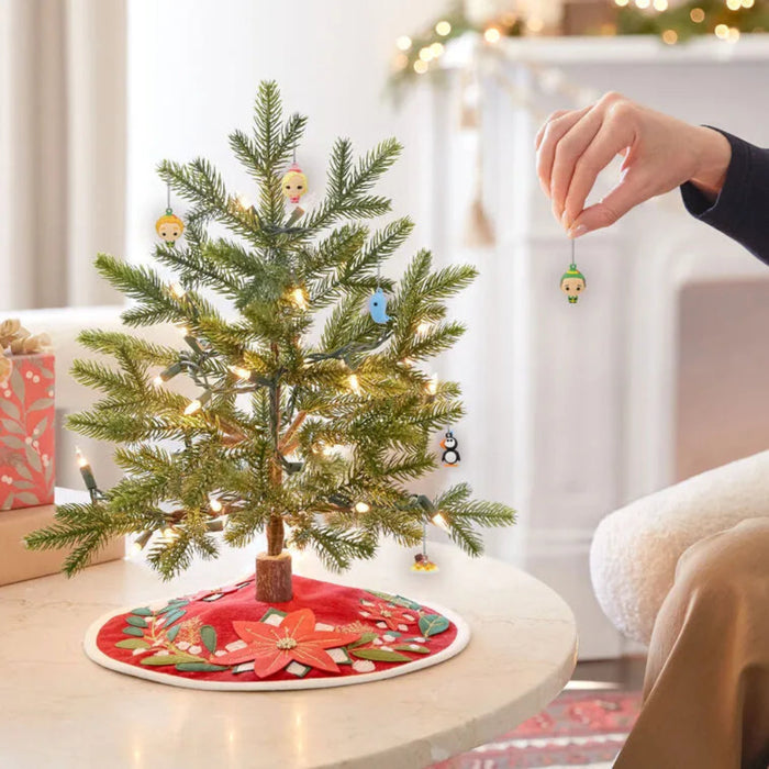 Small decorated  elf themed Christmas tree on a table with a person adding an ornament.