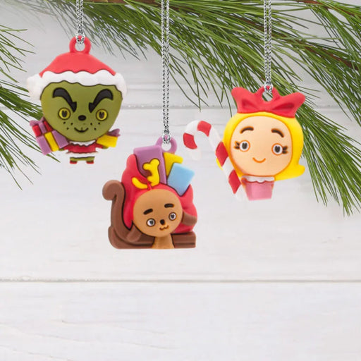 Three colorful Grinch Christmas ornaments hanging on a branch with a white background