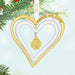Heart-shaped ornament with gold border and pendant, hanging against a green Christmas tree background.