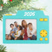Turquoise camera-shaped photo ornament with '2026' and a family photo, hanging on a Christmas tree.