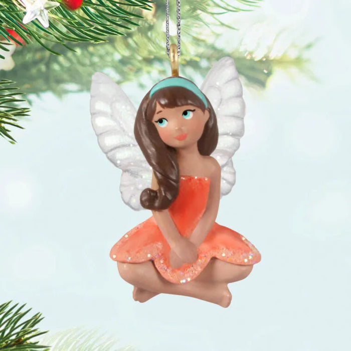 Fairy ornament with white wings and a red dress hanging on a Christmas tree.