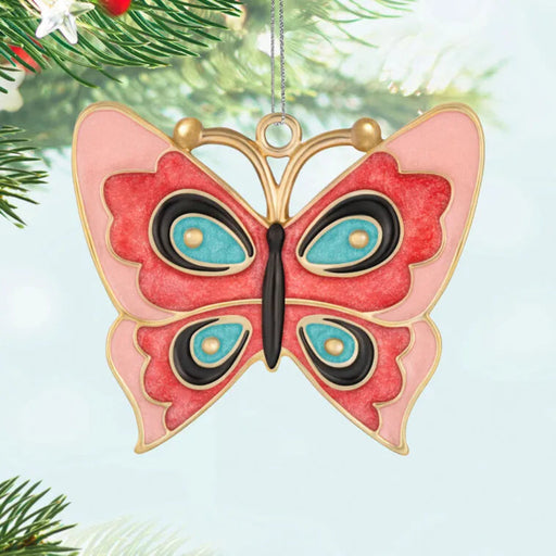 Butterfly-shaped ornament with pink, black, and blue design hanging on a tree.