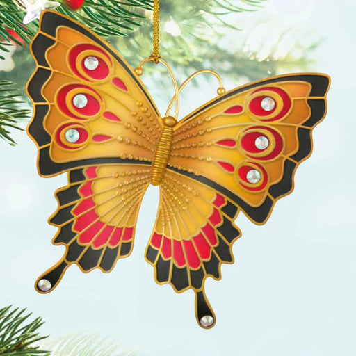 Butterfly-shaped ornament with gold, red, and black colors hanging on a Christmas tree.