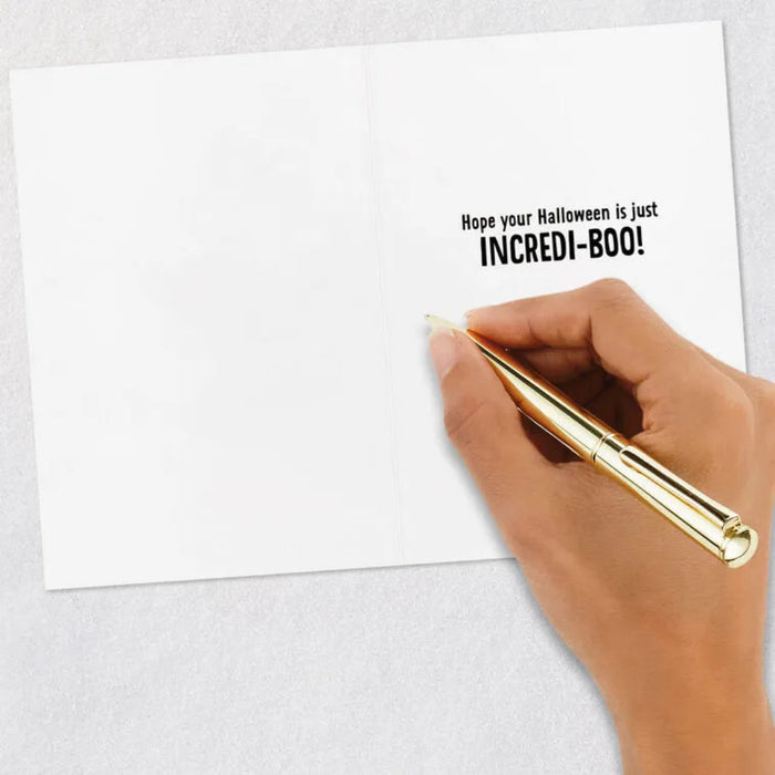 Hand holding a gold pen over a white card with Halloween message on a light gray background