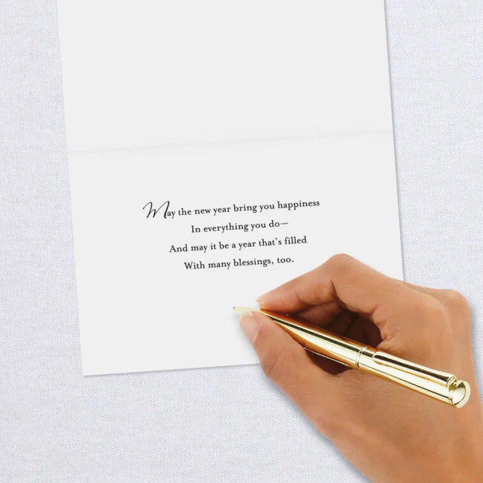 Hand holding a gold pen over a card with a New Year's message on a light gray background