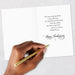 Hand holding a gold pen over a Thanksgiving card with a message on a light gray background