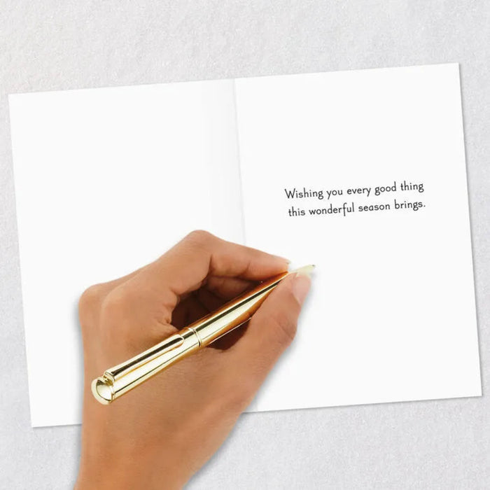 Hand holding a gold pen over a greeting card with a message on a light gray background
