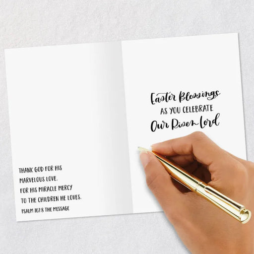 Hand holding a gold pen over an open card with Easter blessings text.