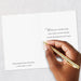 Hand holding a gold pen over a white card with text on a light gray background