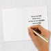 Hand holding a gold pen over a white card with a motivational message on a light gray background