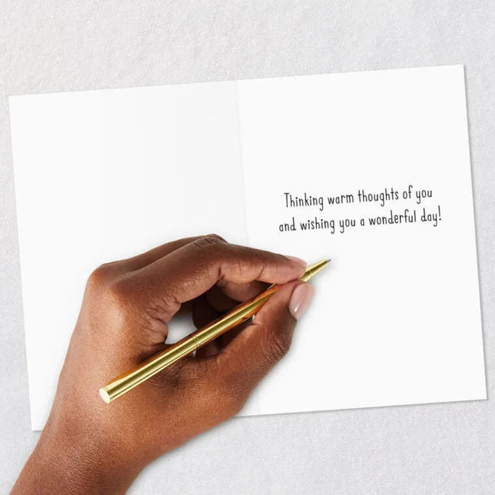 Hand writing on a card with a gold pen, text 'Thinking warm thoughts of you and wishing you a wonderful day.'