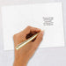 Hand holding a gold pen over a white card with text on a light gray background